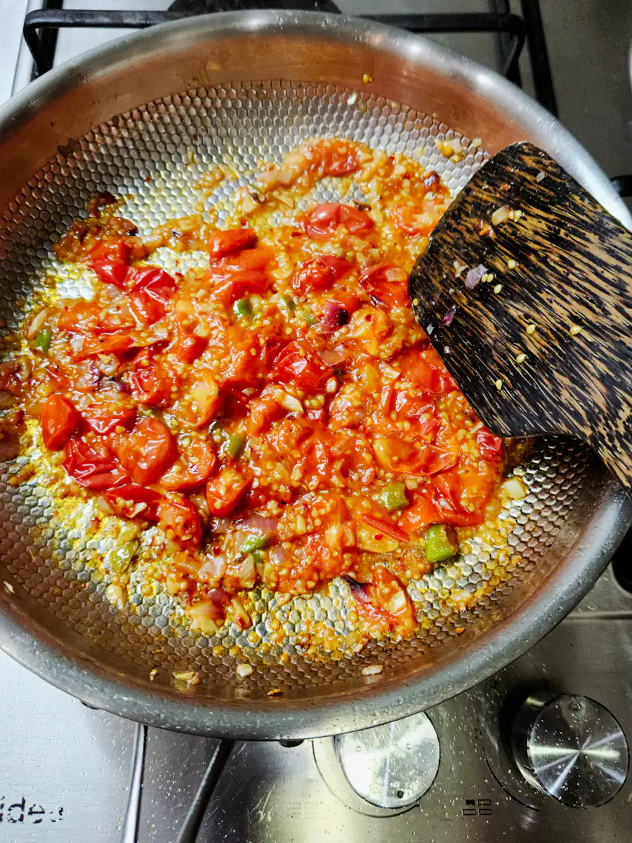 Tomate e cebola a reduzir numa frigideira, mexidos com uma espátula de madeira