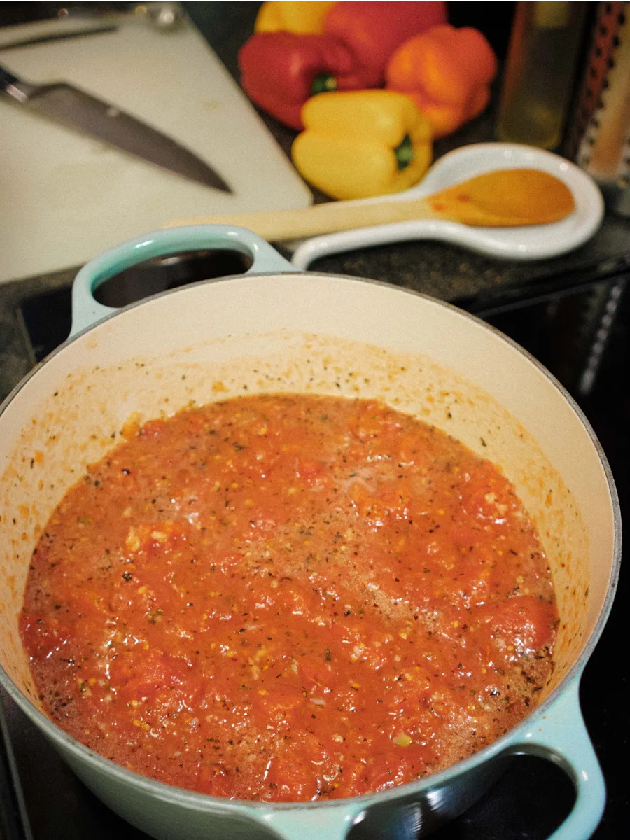 Molho de tomate temperado com ervas numa panela, com pimentos ao fundo