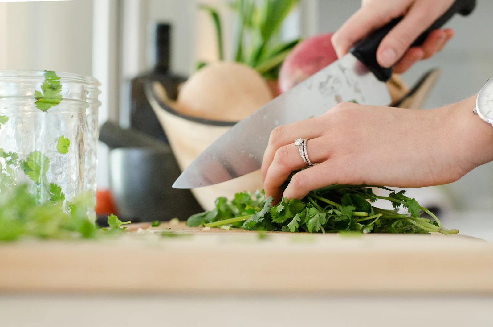 Mãos a picar coentros com uma faca de chef numa tábua de madeira